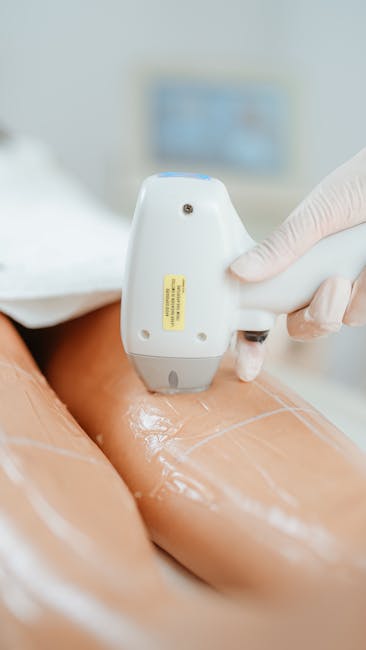 A close-up view of a person wearing a white glove using a handheld ultrasound device on a person's thigh, with a shiny, gel-like substance applied to the skin. The background displays a blurred white and blue medical environment with a monitor or screen partially visible. In a house removal context supported by Man with Van Downham, this image illustrates professional preparation or medical cleaning procedures involved during a home relocation, emphasizing the importance of careful handling and hygiene during packing or client care activities related to removals services.